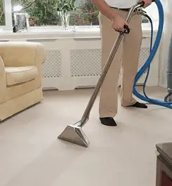 Professional carpet cleaner using a hot-water extraction wand and hose machine in a living room in San Diego, CA.