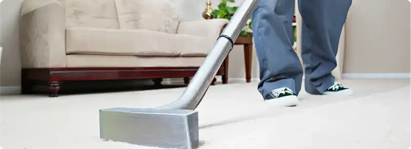 Carpet cleaning technician using a hot-water extraction wand on a light-colored carpet in a living room, San Diego, CA.