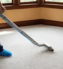 Steam carpet cleaning technician using a hot-water extraction wand on a residential carpet, wearing blue protective shoe covers San Diego, CA.
