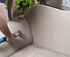 Professional upholstery cleaner deep-cleaning a fabric sofa with a handheld extraction tool and hose in San Diego, CA.